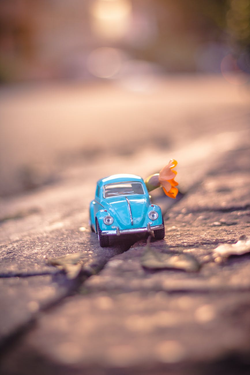 A tiny blue toy VW beetle with a small yellow flower stuffed into it.