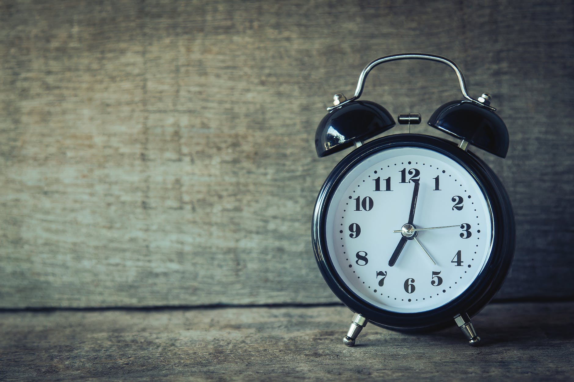 Traditional analogue alarm clock with the hands pointing to two minutes past seven.
