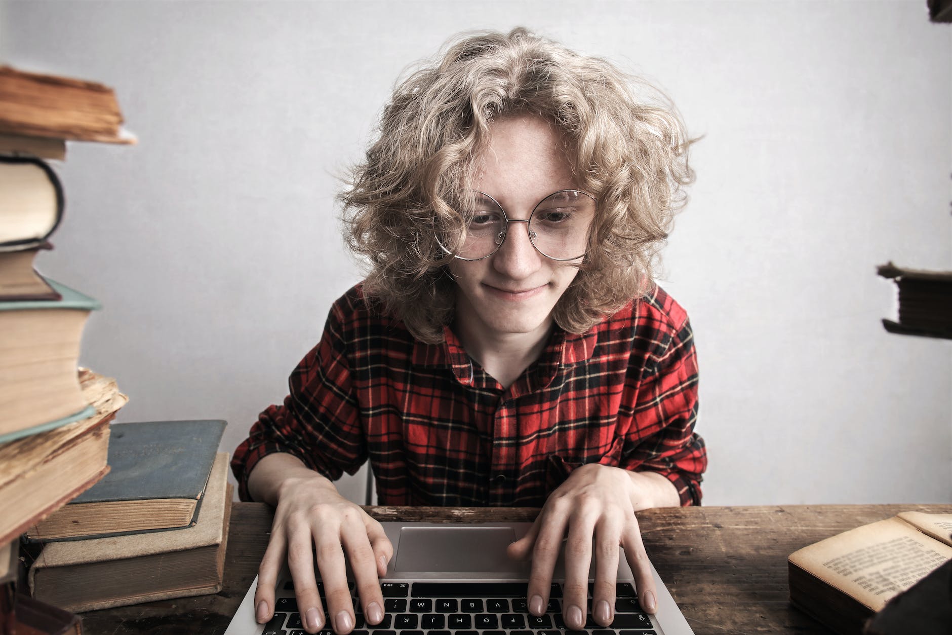 Geeky looking person working on a laptop next to piles of books