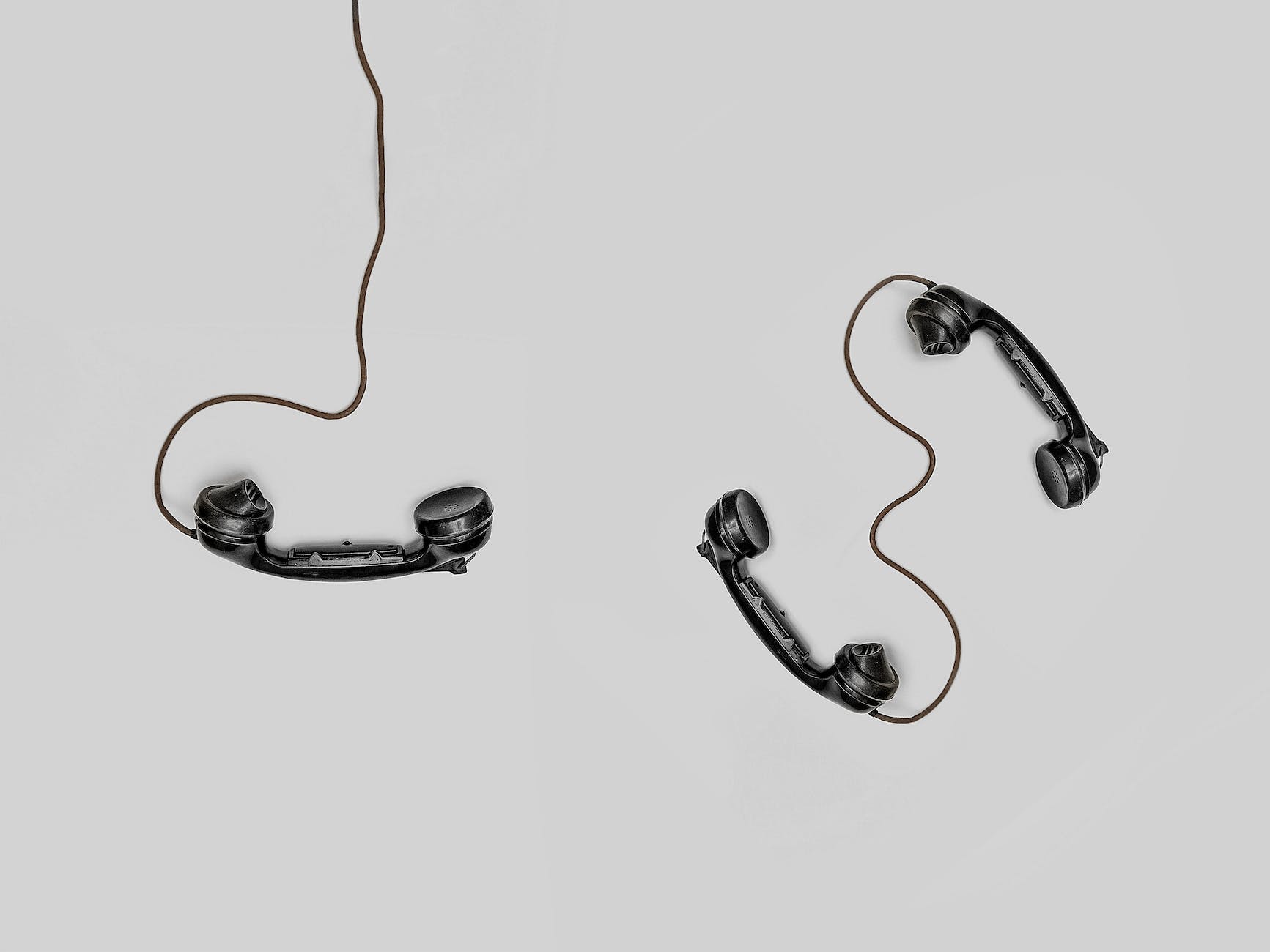 Overhead shot of three black old school wired telephones against a white background. 