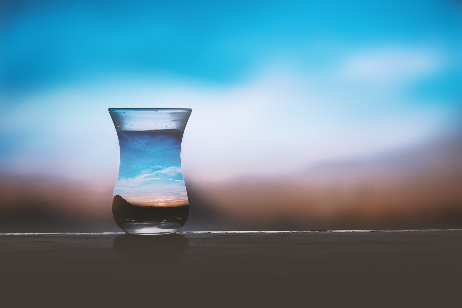 A glass of water taken against a blurred horizon so the image in the glass is focused.