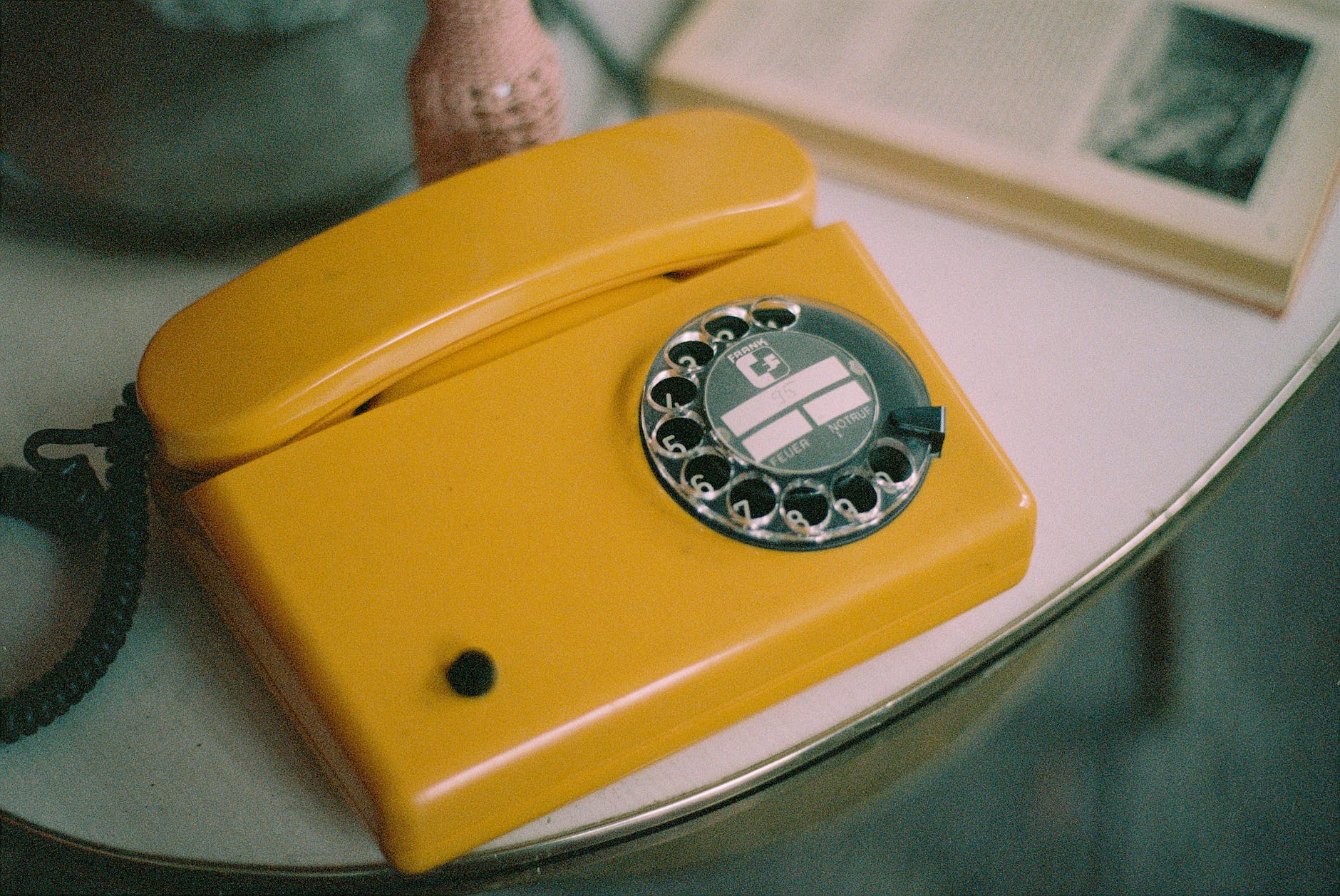 Close up of a yellow analogue dial up phone sitting on a white laminated table.