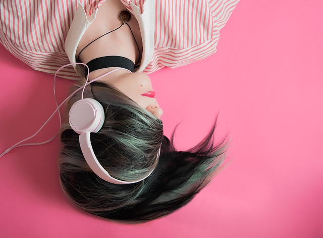 Picture of a girl from the shoulders up in a pink and white striped shirt listening to headphones. Her hair overs her eyes and she's upside down against a bright pink background.