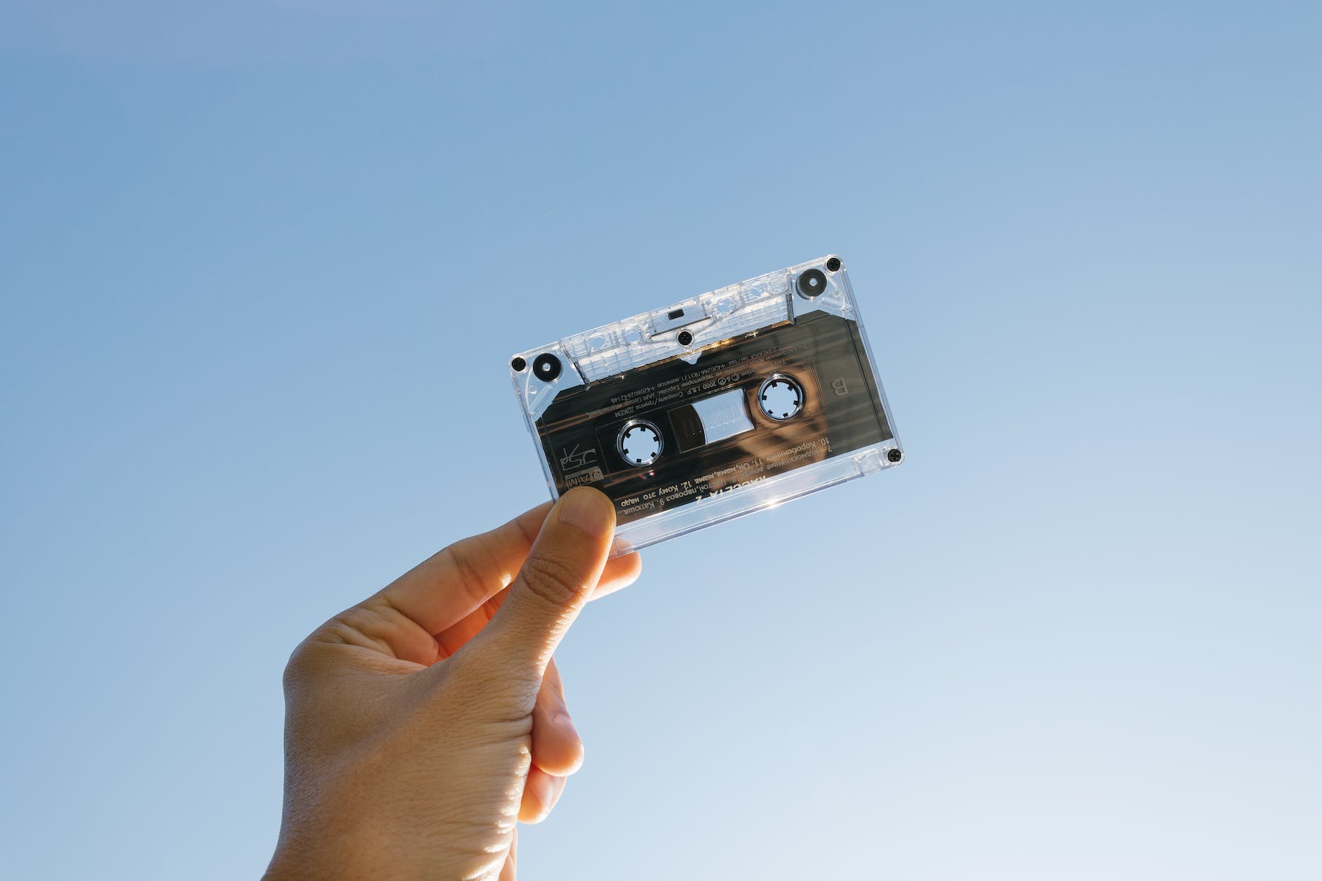 A hand holding a music cassette tape up in the air against a blue sky