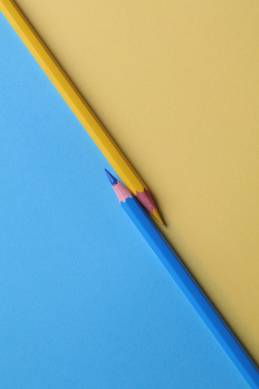 A blue and a yellow pencil facing each other diagonally on a blue and yellow background