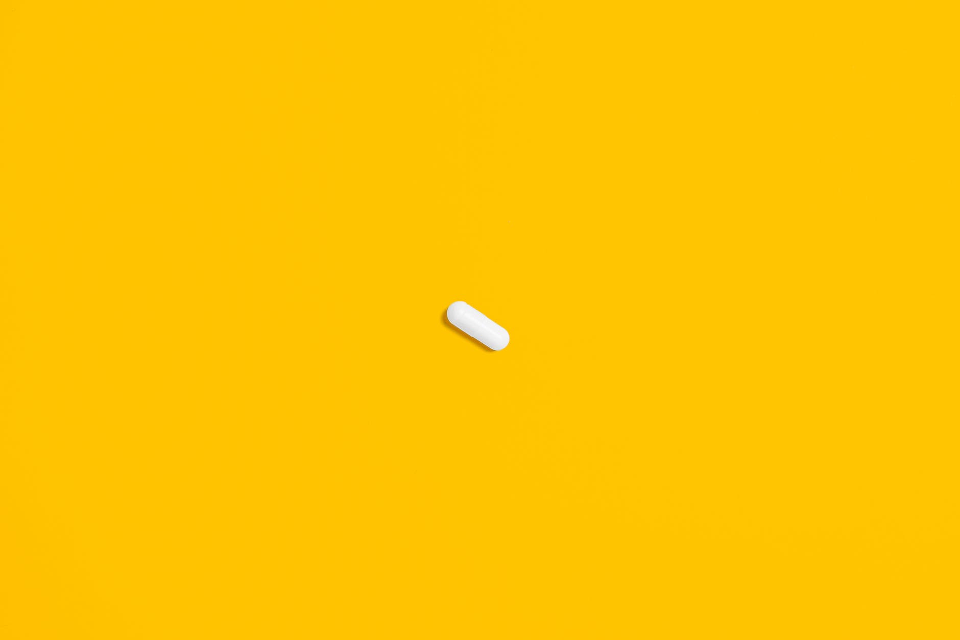 A single white pill on a yellow background