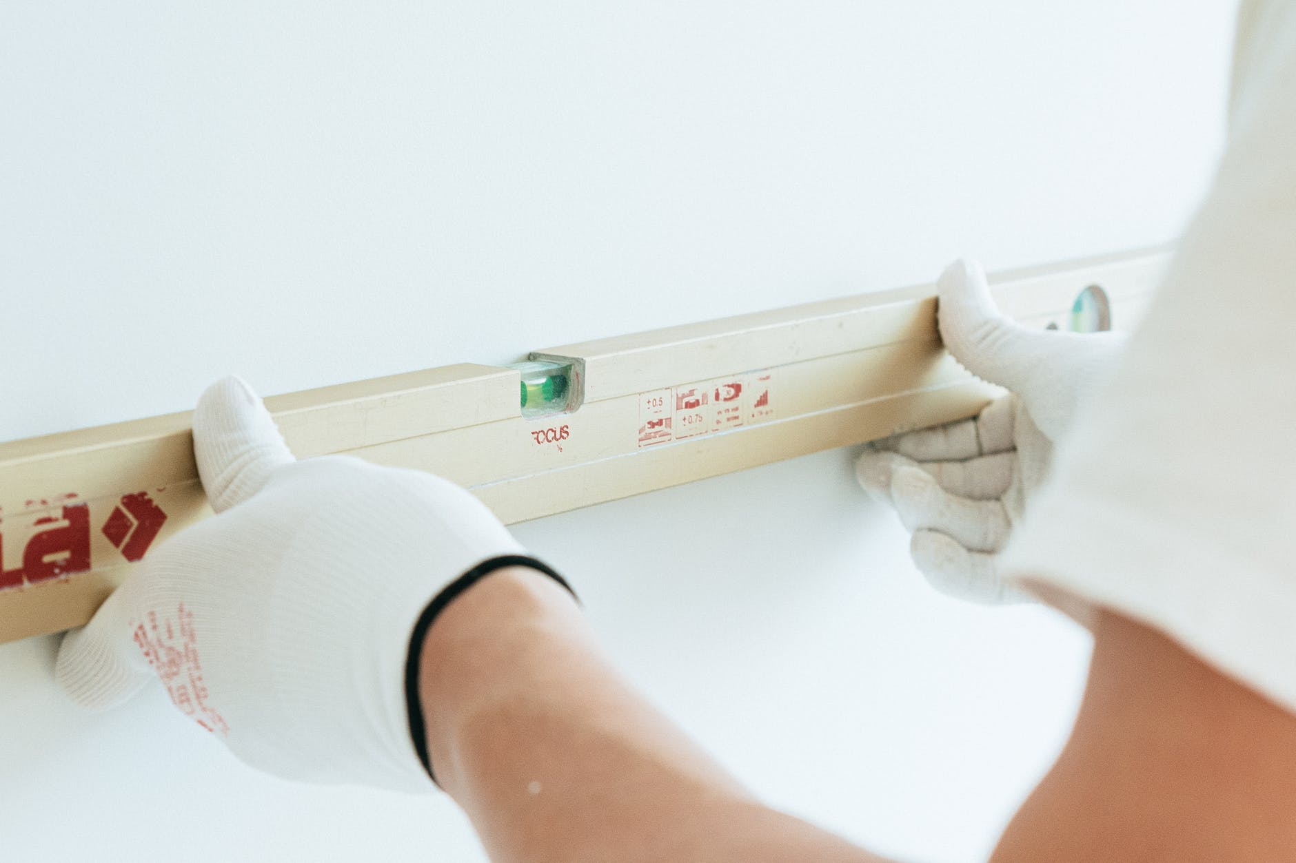 A gloved person pressing a spirit level up against a white painted wall.