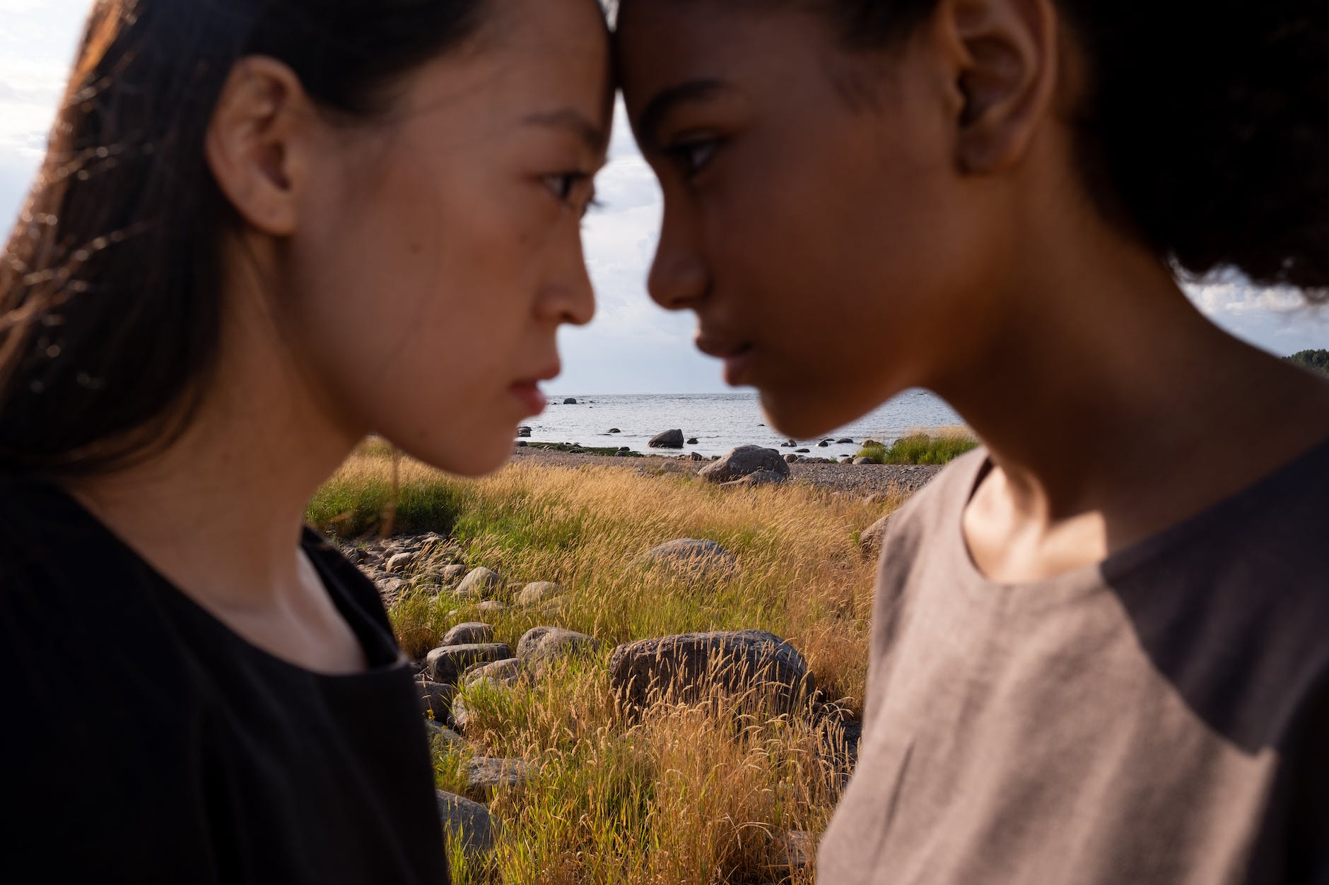 Two women, foreheads touching, with a grassland and water in the background