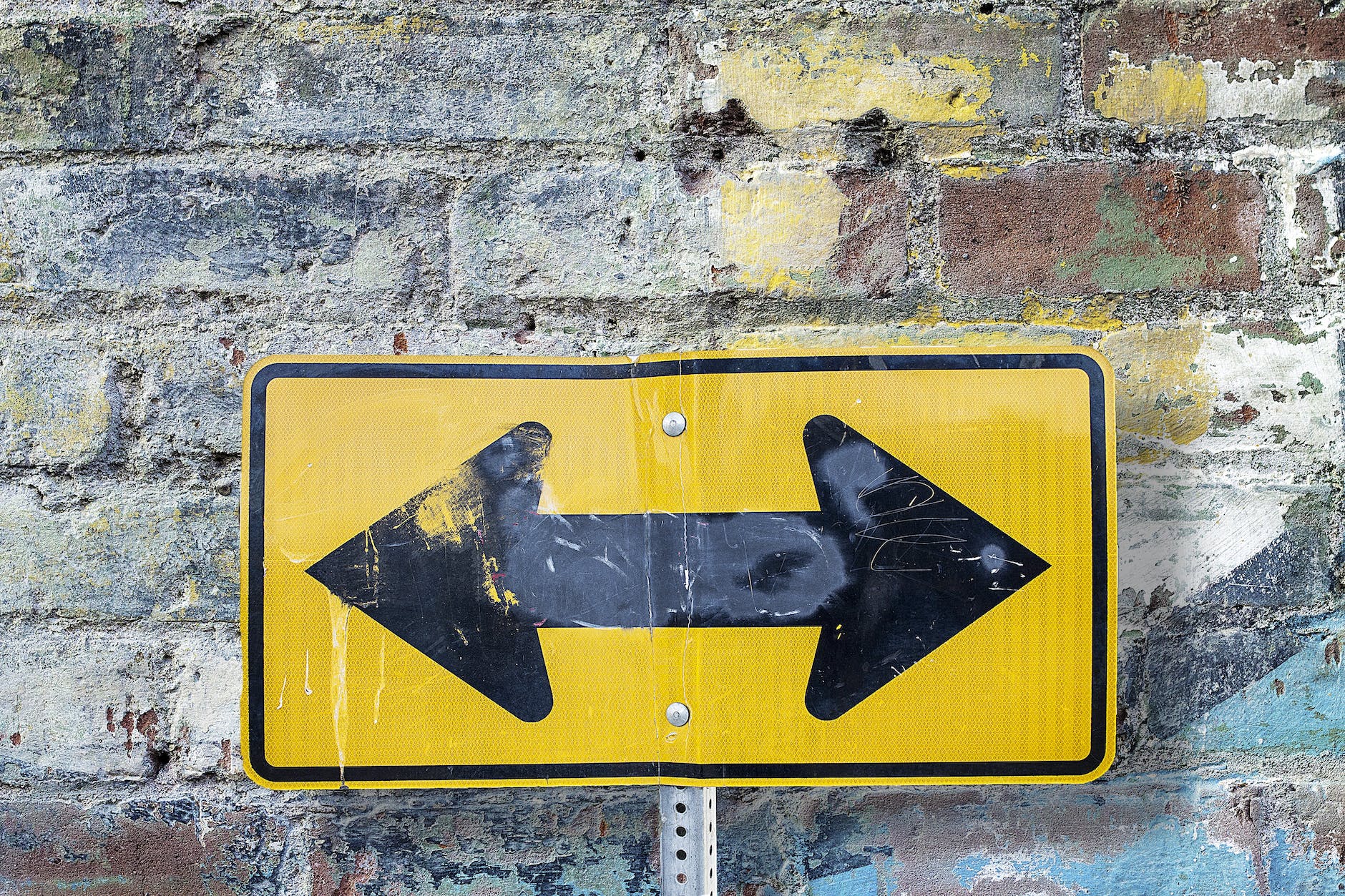 Black double arow on a yellow background up against a brick wall.