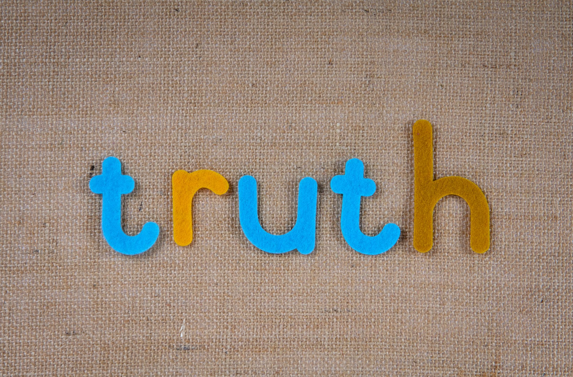 Letters made of blue and brown felt spelling 'truth' against a hessian background
