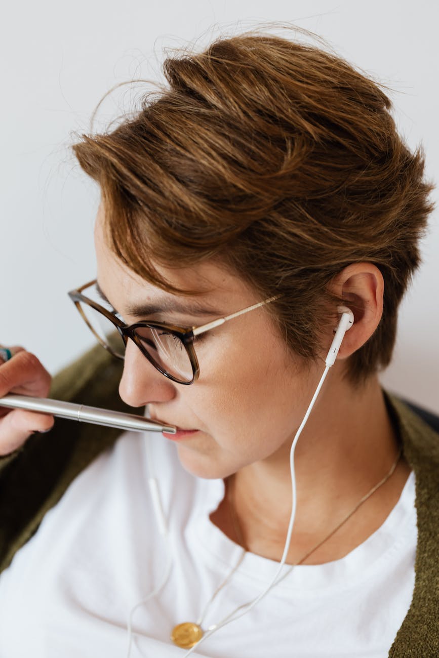 Woman with white headphones, thinking with a pen held to her mouth.