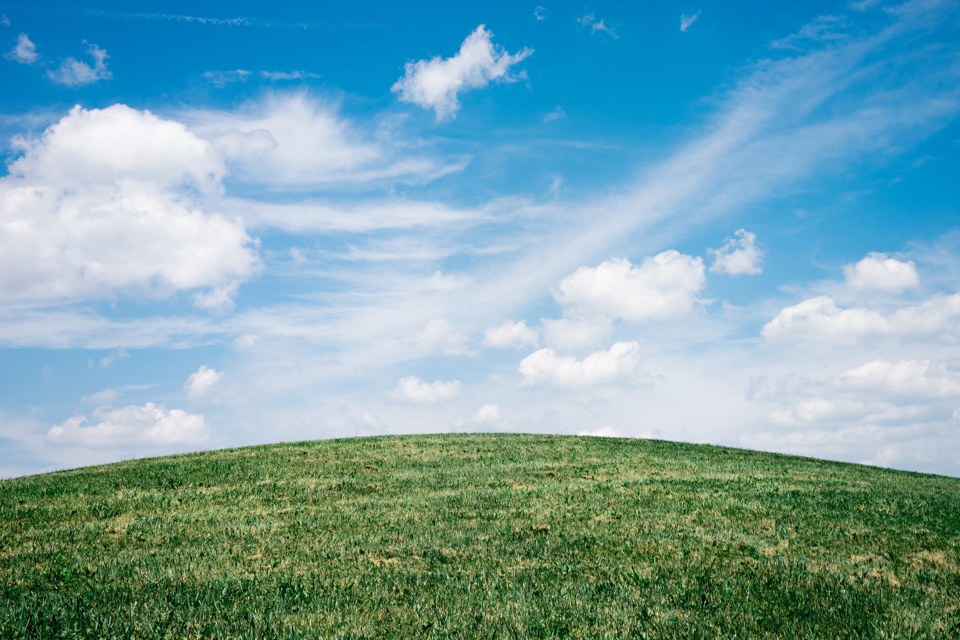 Image of a green hill to the horizon. The blue sky has a few white fluffy clouds.