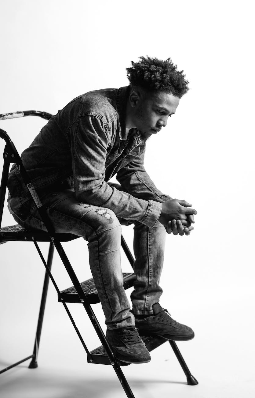 Black and white picture of a black man man sitting on a step ladder thinking.