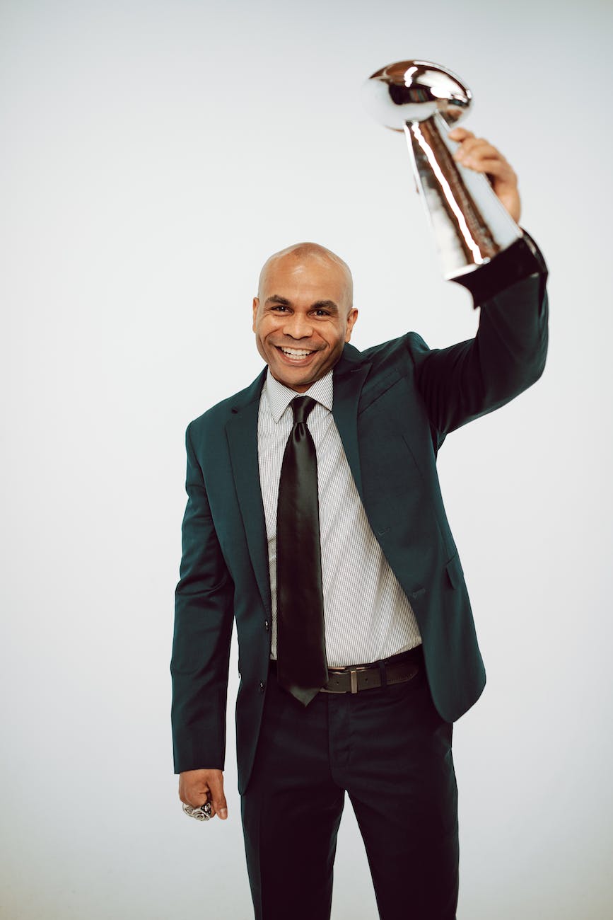 A Man in Green Suit Holding a Trophy while Looking at the Camera
