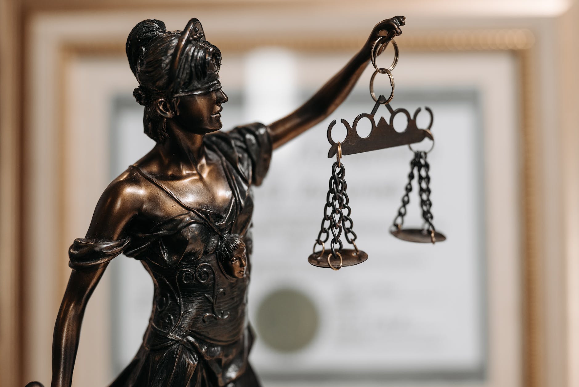 The image depicts a bronze statue of Lady Justice, a personification of the moral force in judicial systems. She is blindfolded, representing objectivity and impartiality, holding a sword and a set of scales, symbolizing the power of reason and justice.