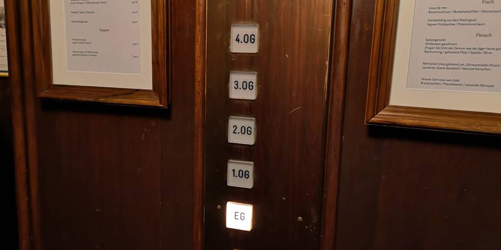 A lift panel with buttons for floors EG, 1.OG, 2.OG, 3.OG, 4.OG, and framed menus on the wall in a wooden interior.