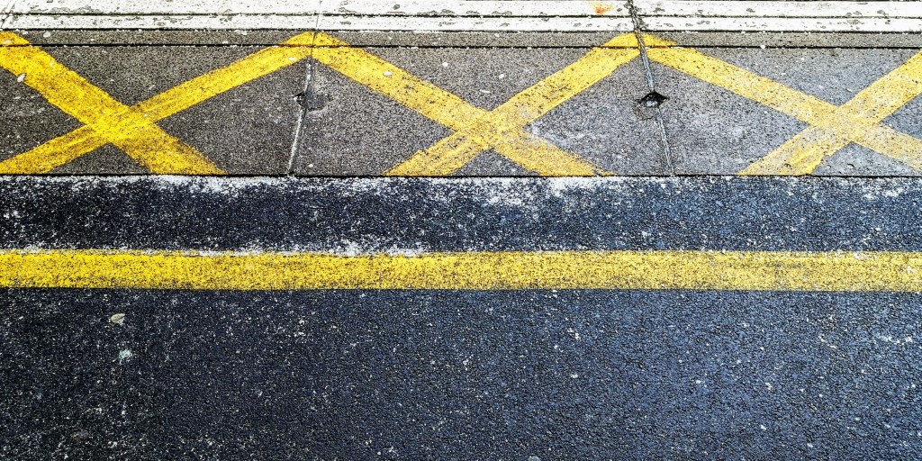 A train platform with a textured surface featuring yellow safety lines and a crosshatched no-standing zone.