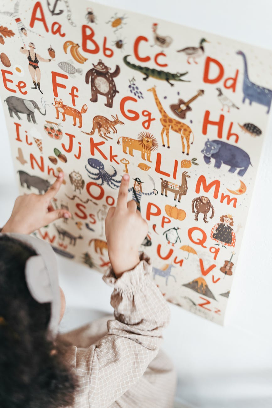 A child points to letters on a colourful alphabet chart with animal illustrations.

