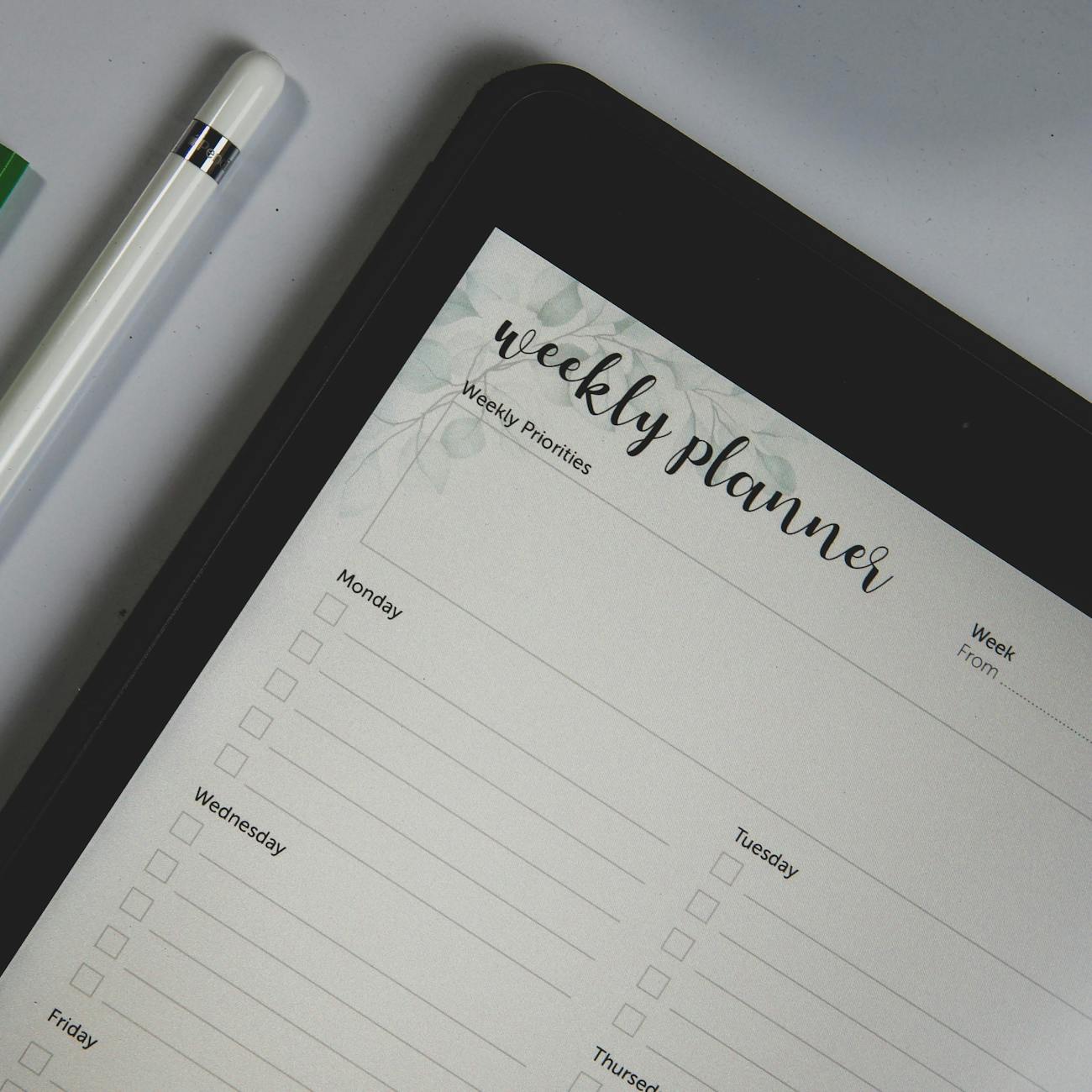 The image shows a weekly planner tablet with unfilled dates and tasks. A white stylus pen rests beside it.