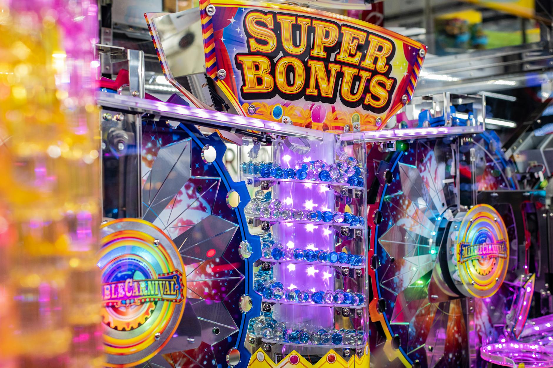 The image shows a vibrant, colorful slot machine or arcade game called "Super Bonus". It is decorated with bright lights, rainbow patterns, and various star and circular shapes, displaying a lively and eye-catching carnival-style aesthetic.

