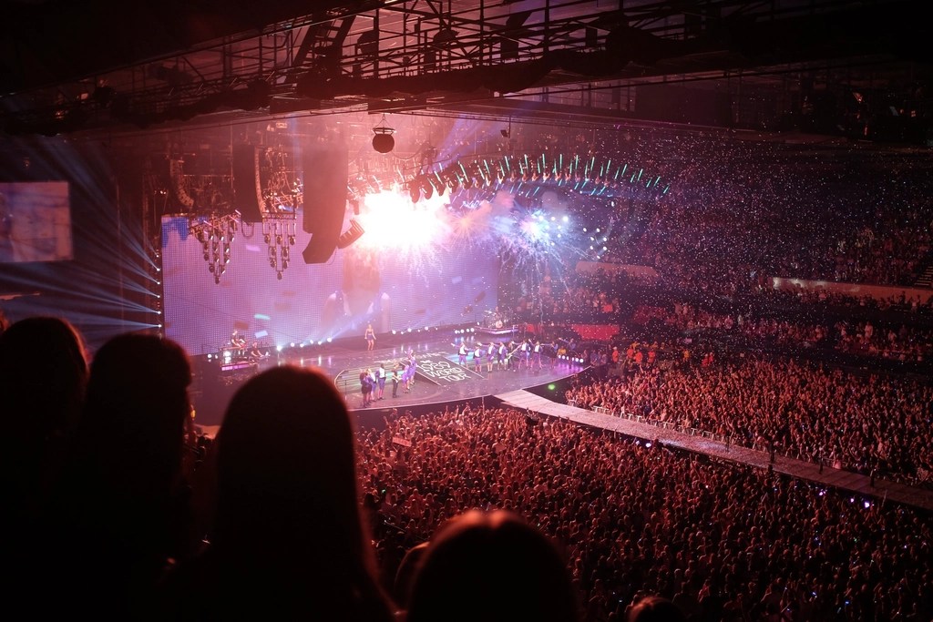 This image captures a vibrant concert scene with a large audience and a brightly lit stage. It is from the Taylor Swift 1989 tour.