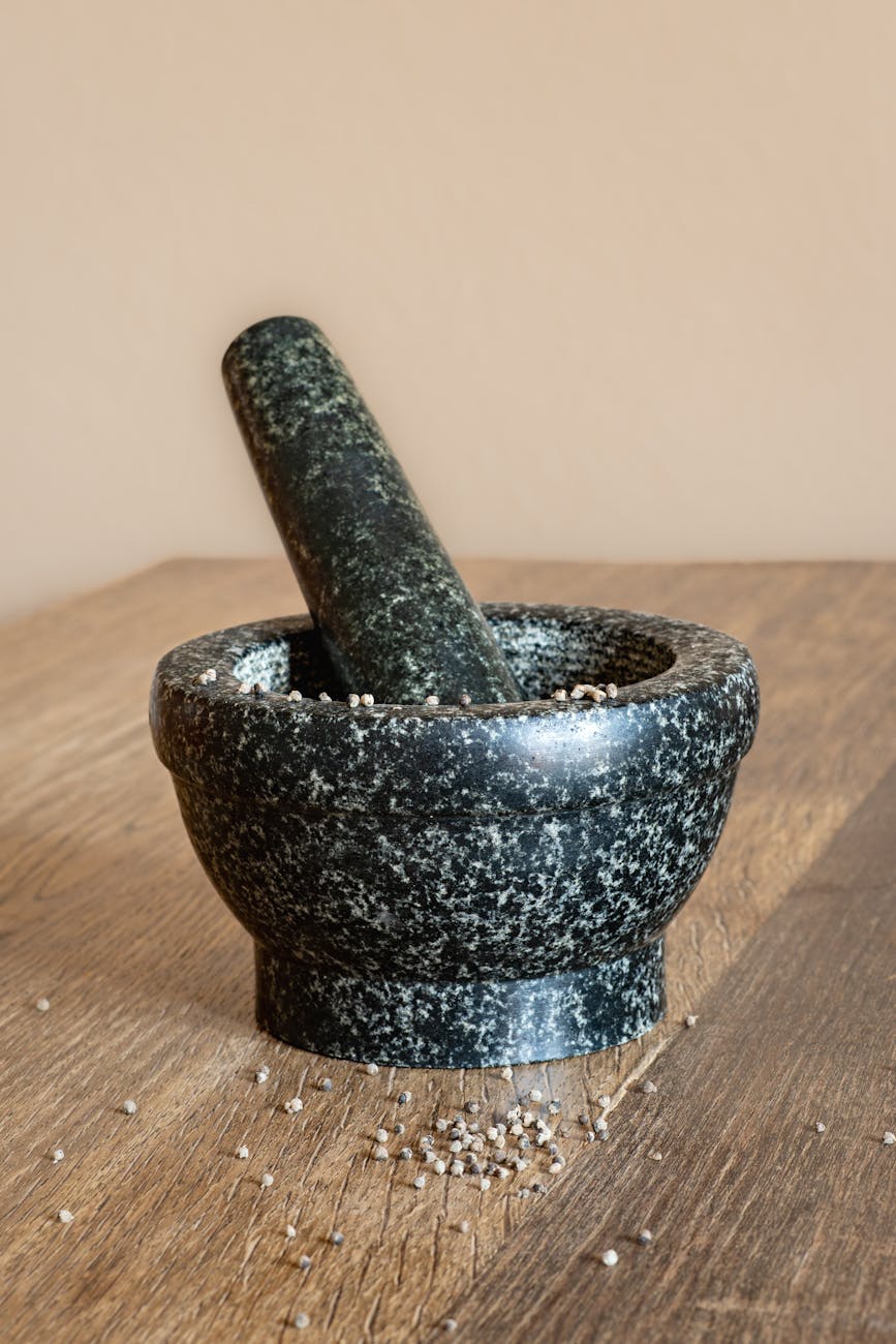 The image shows a textured stone mortar and pestle on a wooden surface, suggesting traditional food preparation.