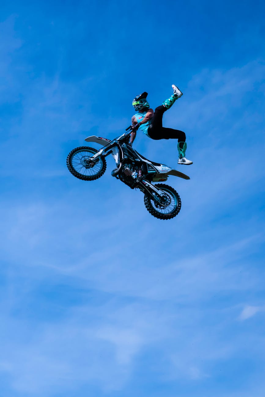Airborne motocross rider performing a stunt against a clear blue sky.

