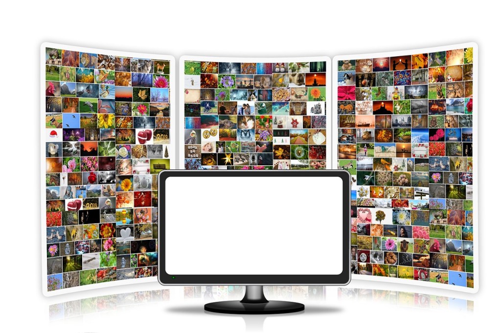 A computer monitor in the foreground with a blank white screen. Behind the monitor, there are three large panels filled with numerous small images or thumbnails, creating a collage effect. The images appear to be a mix of nature, animals, landscapes, and various other subjects, arranged in a grid format on each panel.