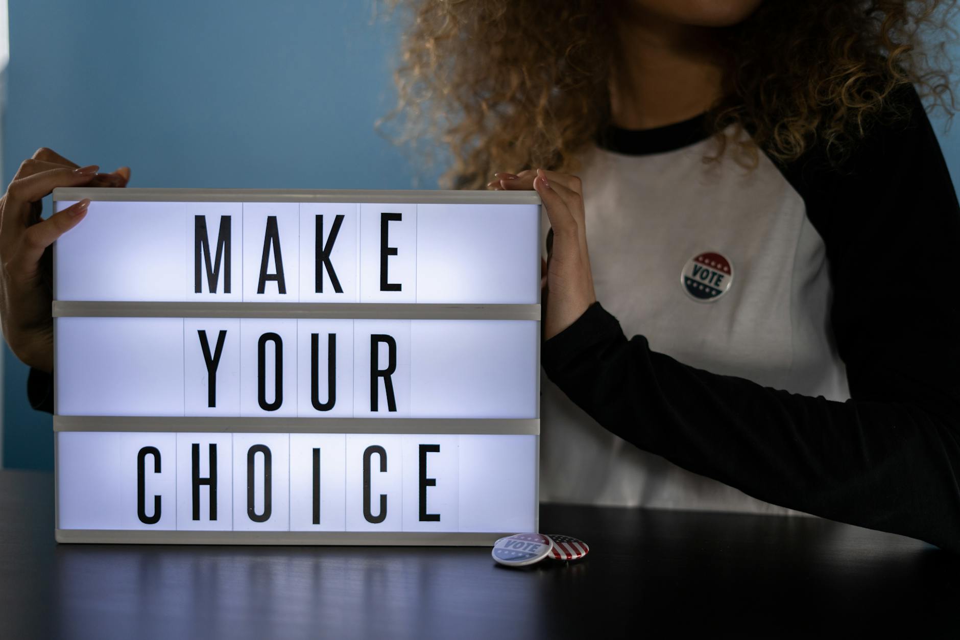 The image shows a person holding up a light box displaying the text "MAKE YOUR CHOICE".