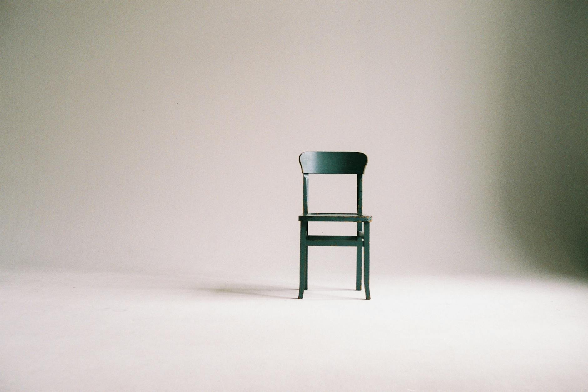 A single wooden chair placed in the centre of a minimalist setting with a plain background.