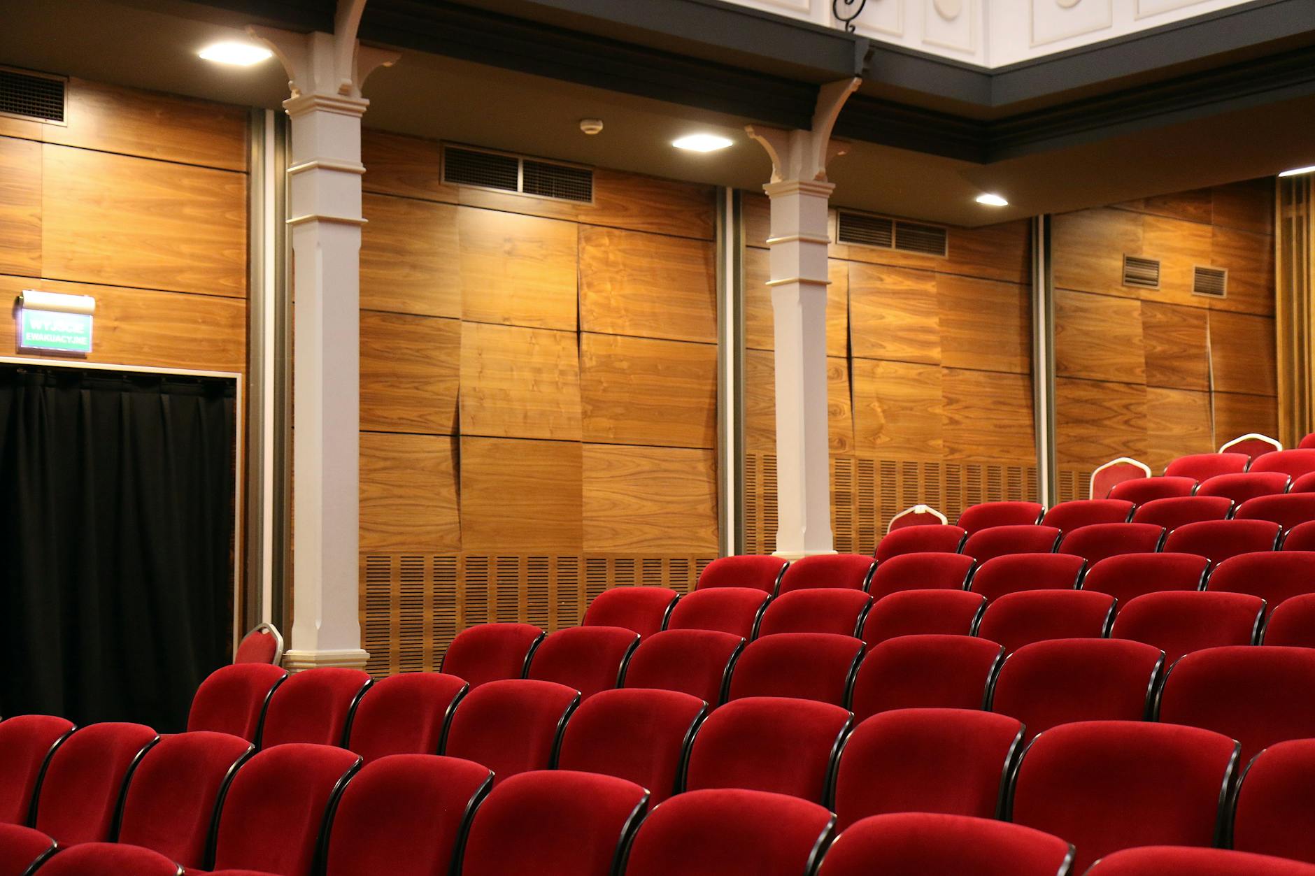 Rows of red upholstered seats in a theatre or auditorium with wooden panelling on the walls and overhead lighting