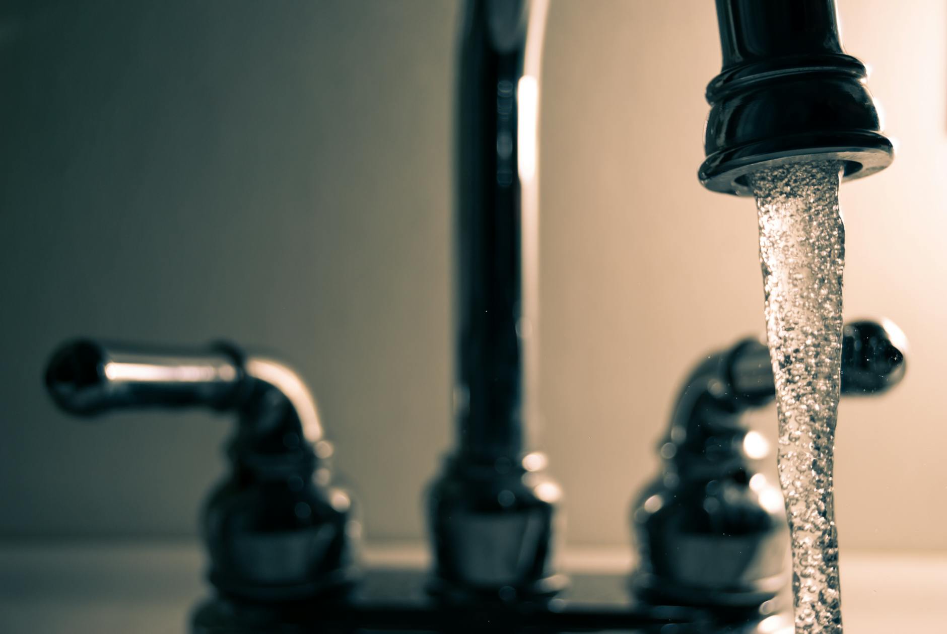 Close-up of water flowing from a chrome tap with soft-focus background, highlighting the contrast between the clear water stream and blurred surroundings.