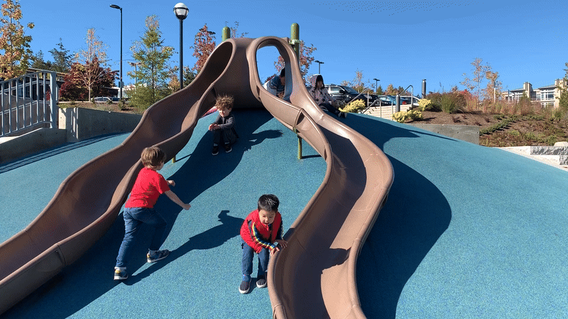 A gif of children playing on a slide in a playground. None are using the slide but the hill it is built on.