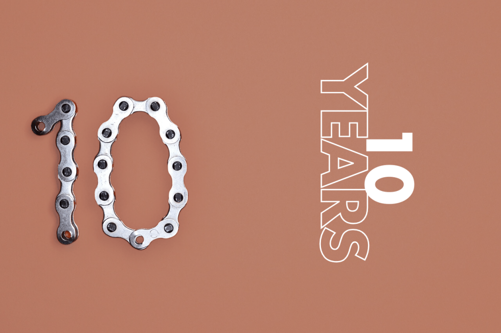 A bicycle chain is arranged to form the number "10" on a brown background, with the text "10 YEARS" in stylized letters on the side.