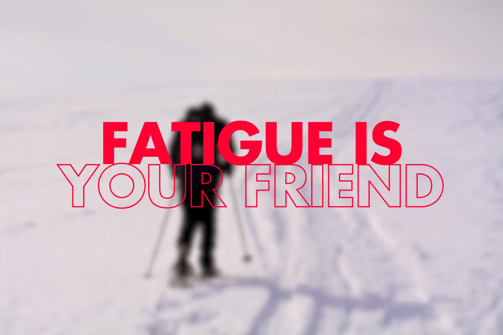 "A silhouetted figure with trekking poles walks away from the viewer on a snowy, white landscape. The text overlay reads, 'FATIGUE IS YOUR FRIEND,' with 'FATIGUE IS' in a bold, outlined font and 'YOUR FRIEND' in a thinner, outlined font, both in a reddish colour."