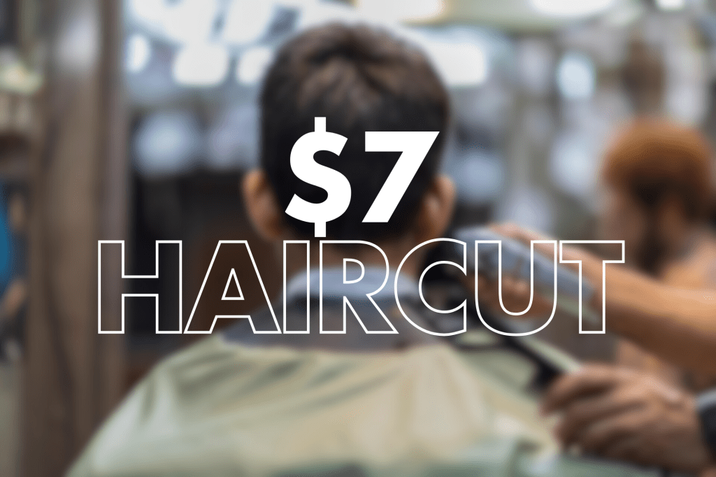 The image shows a blurred background of a barbershop or salon setting with the text "$7 HAIRCUT" prominently displayed in large, bold white letters over the scene. A person is sitting in a barber's chair.