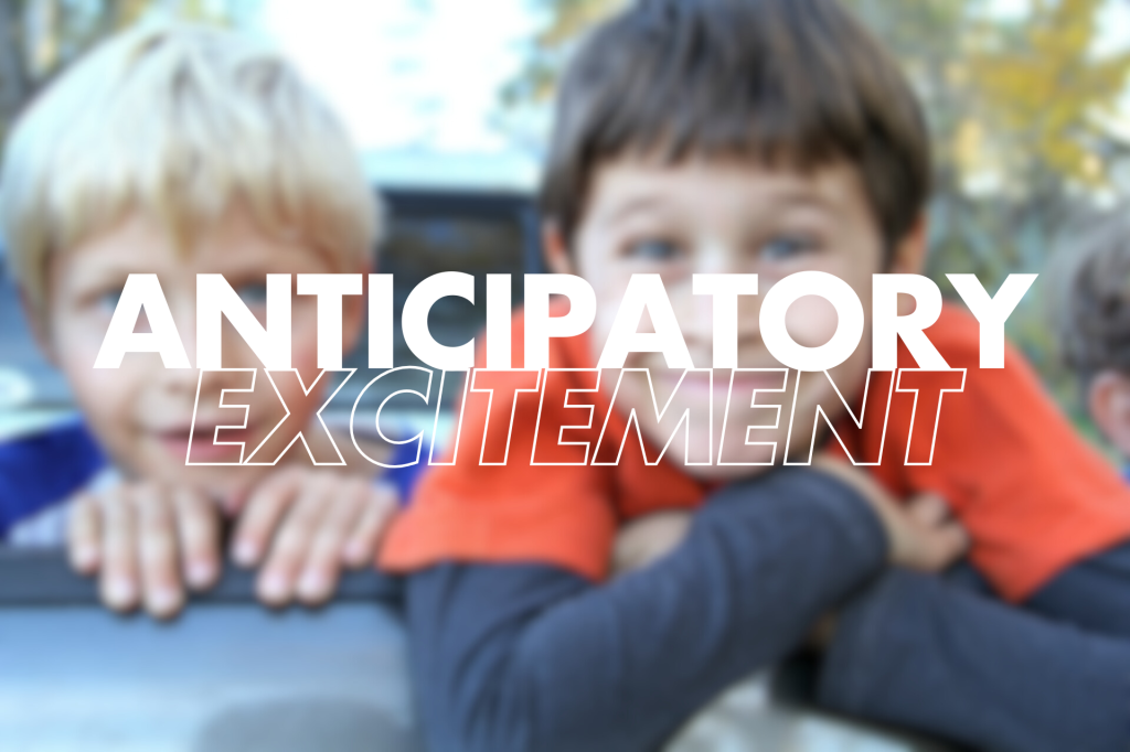 he image shows the phrase "ANTICIPATORY EXCITEMENT" in large, white, slightly outlined capital letters superimposed on a blurred background of two children. The child on the right is looking directly at the camera with a slightly eager expression.
