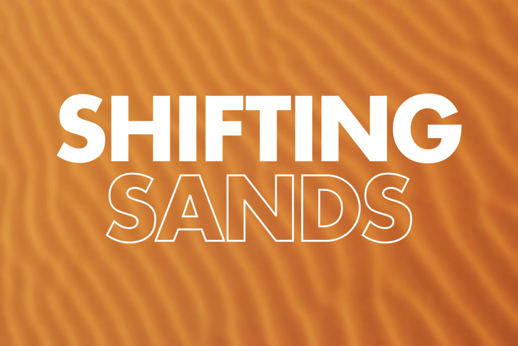 White text reading "SHIFTING SANDS" overlaid on an orange background with curved, flowing sand dune patterns creating a desert landscape effect.