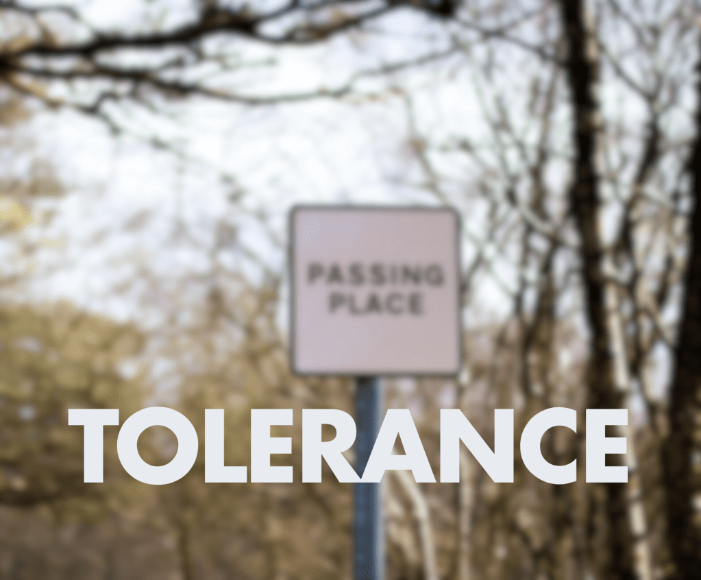 A blurred image of a road sign that says "PASSING PLACE," with the word "TOLERANCE" prominently displayed in large, bold white text at the bottom.