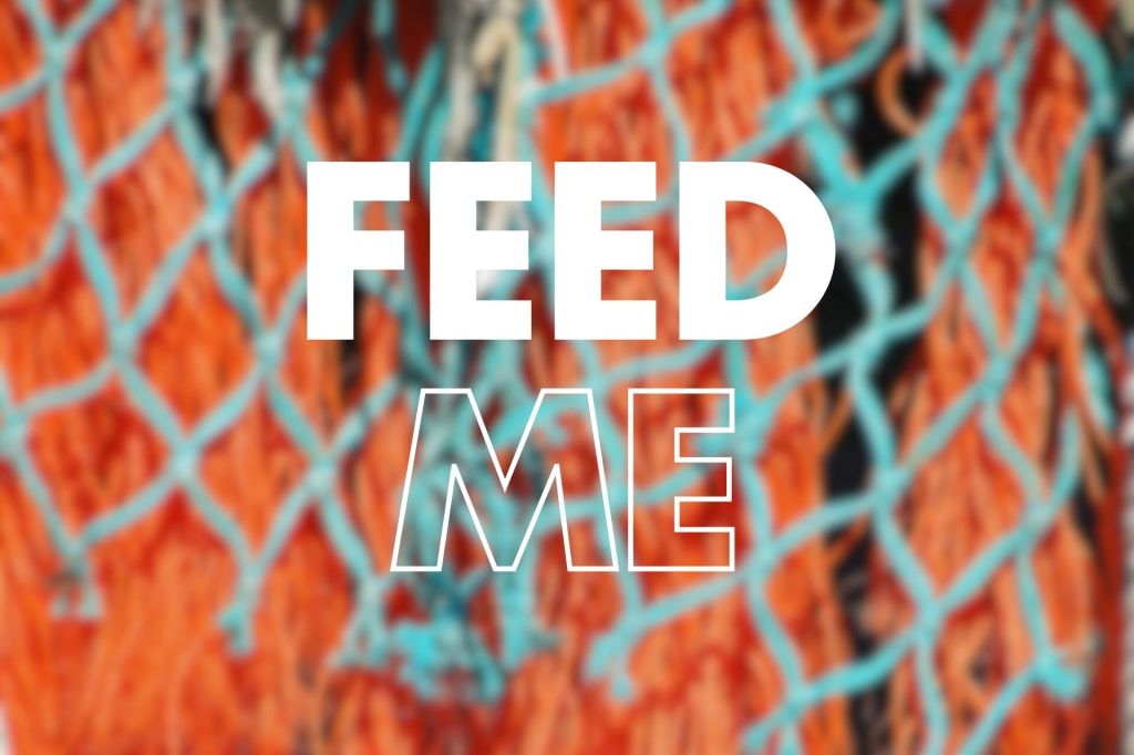 A blurred image of a colourful nets with orange and blue strands, featuring the words "FEED ME" prominently displayed in large, bold white text.