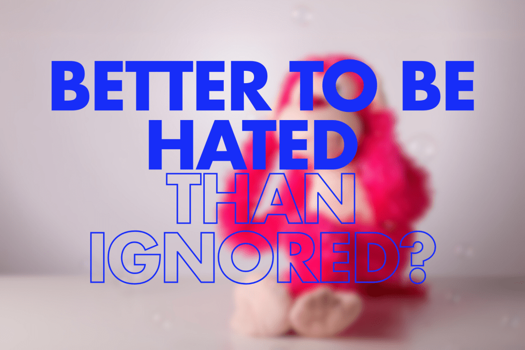 A blurred image of a pink stuffed animal on a light background, featuring the words "BETTER TO BE HATED THAN IGNORED?" prominently displayed in large, bold blue text.