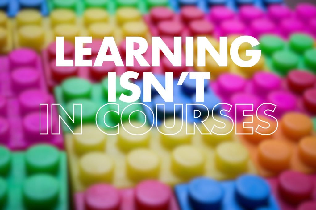 A blurred image of colorful building blocks, with the words "LEARNING ISN'T IN COURSES" prominently displayed in large, bold white text.