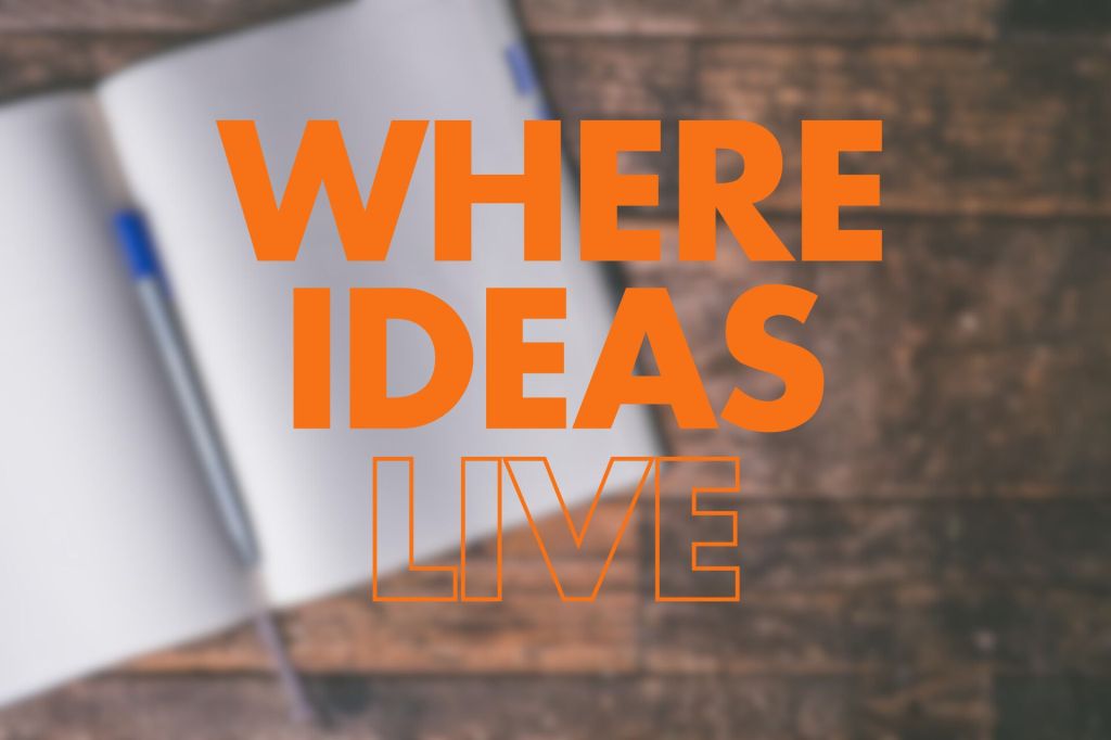 A blurred image of an open notebook with a pen on a wooden surface, featuring the words "WHERE IDEAS LIVE" prominently displayed in large, bold orange text.