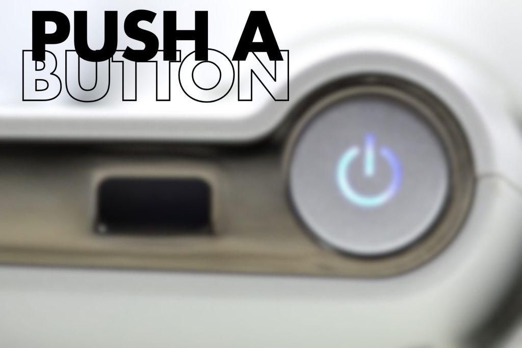Blurry view of an adaptive laptop hinge and keyboard area with a power button icon and a USB-style port; large text reads “PUSH A BUTTON” at the top.

