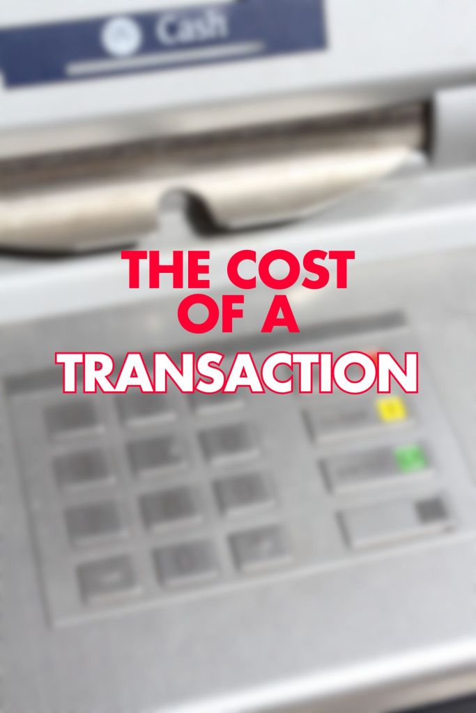 A close-up image of an ATM keypad, slightly blurred, with the phrase "THE COST OF A TRANSACTION" prominently displayed in bold, red letters overlaid on the image. The keypad includes numerical buttons and a cash withdrawal option.


