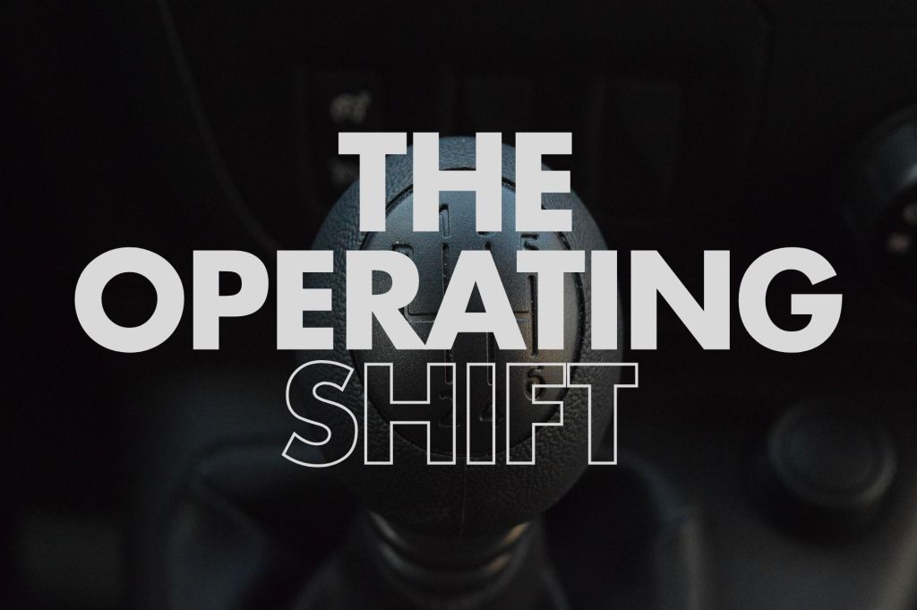 Dark photo of a car manual gear shift, with the knob; large white text overlays read “THE” (top), “OPERATING” (middle), and “SHIFT” (bottom).