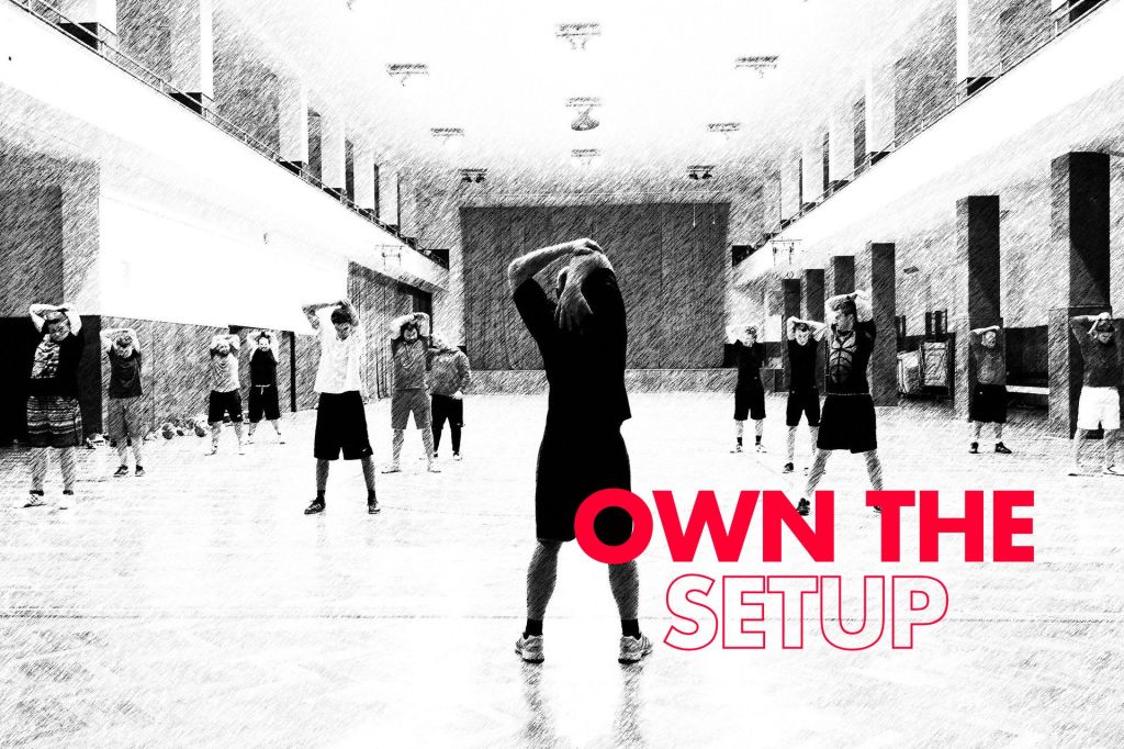 Black and white image of people stretching in a large hall, with red text reading “OWN THE SETUP” in the lower right.